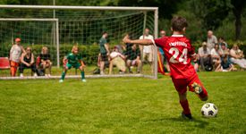Kind steht vor dem Tor und kickt den Ball